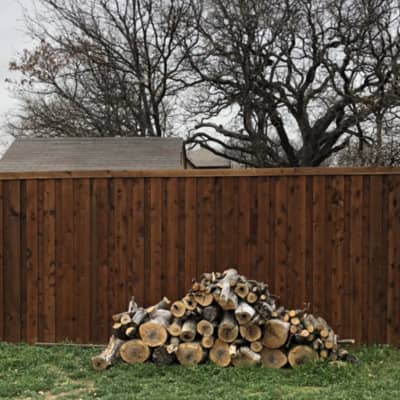 This picture shows a pile of wood in front of a wooden fence recently completed.
